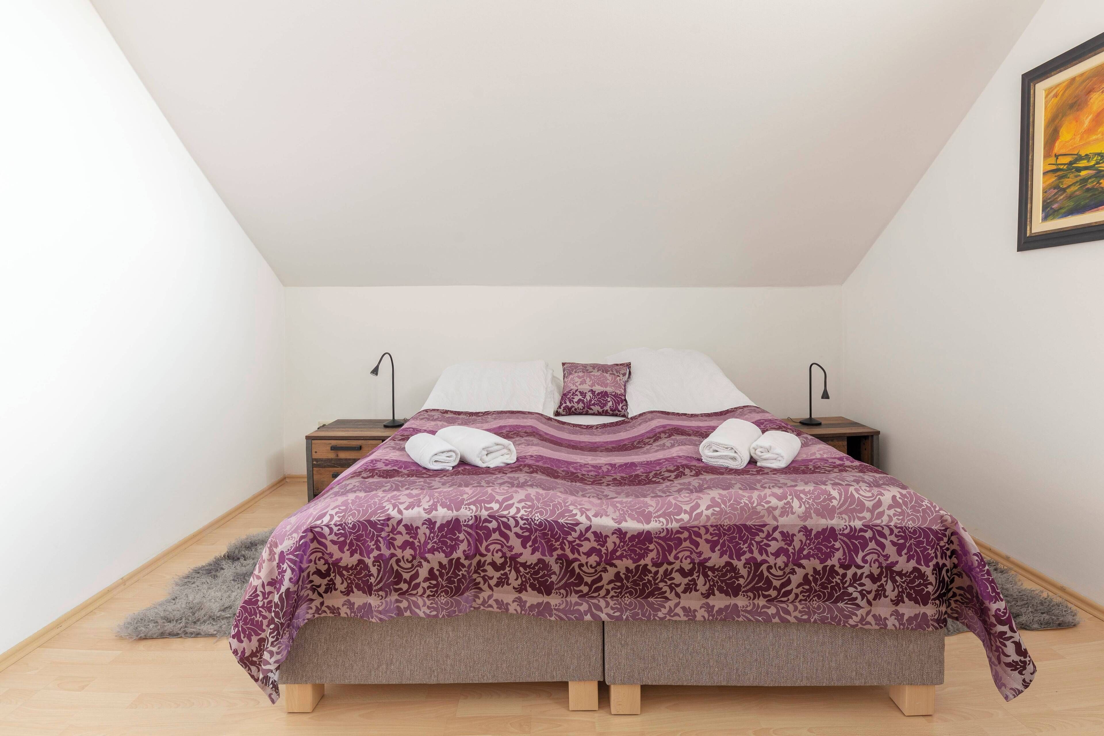 A neatly made bed with a patterned bedspread, two bedside tables with lamps, and a fluffy rug on the floor.