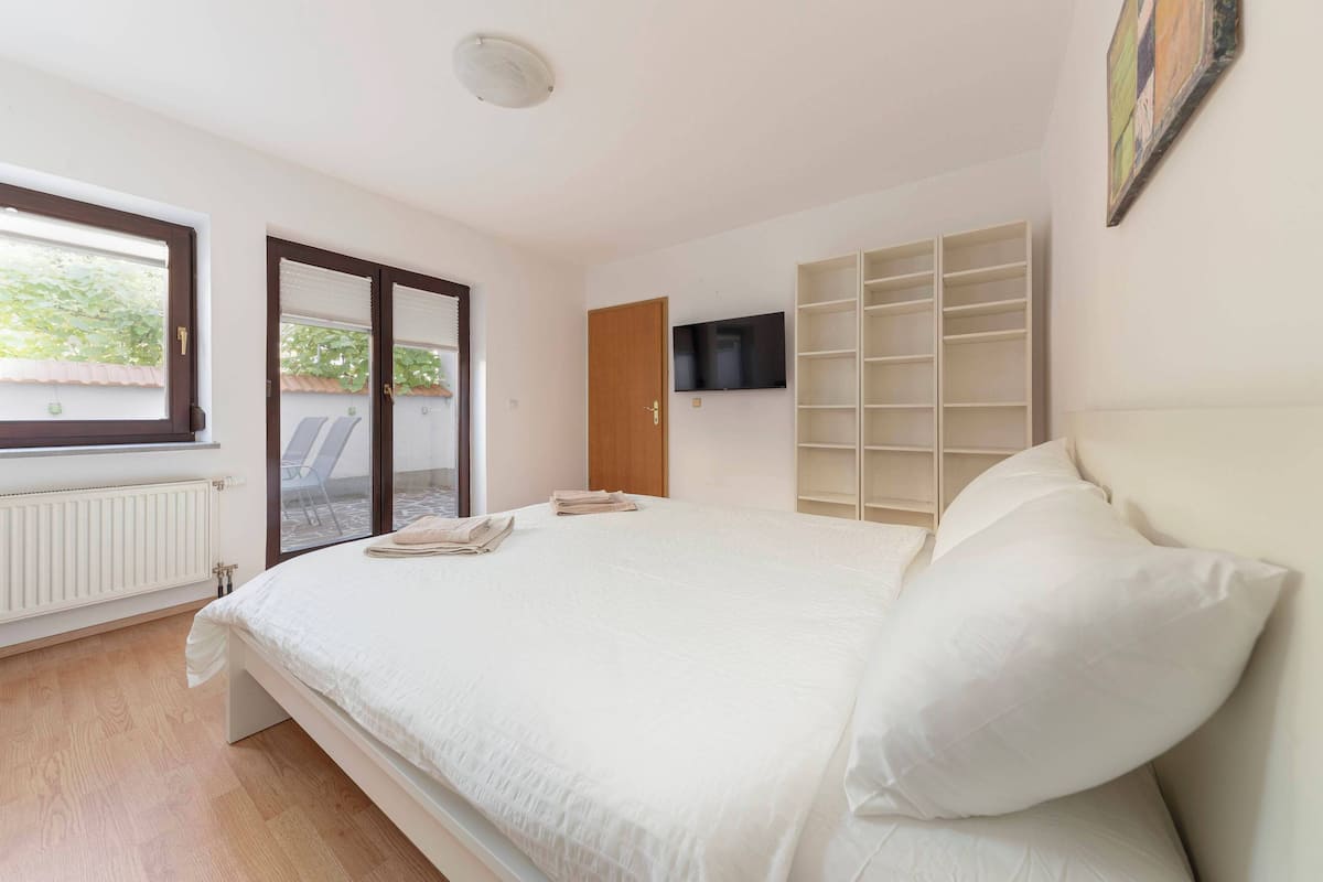Un dormitorio con una cama, televisión, ventana y puerta que da a un balcón.