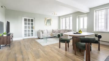 Un salon moderne comprenant un canapé, une table à manger avec des chaises, un téléviseur et une grande fenêtre avec des stores.
