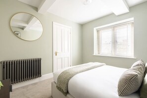 A bedroom with a bed, a radiator, a door, and a window with blinds. - Host & Stay | Caedmons View (Whitby)