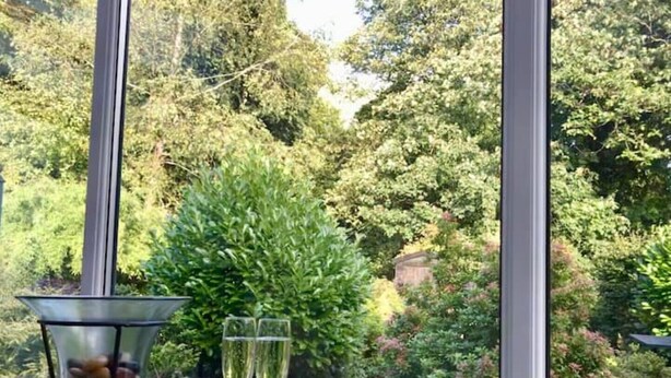 Una mesa con dos copas de champán y un recipiente de vidrio con piedras, frente a un fondo de vegetación exuberante y árboles.