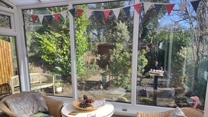 Un invernadero con sillas de mimbre, una mesita y vistas a un jardín.