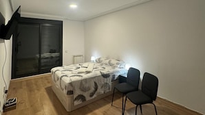 A bedroom with a bed, two chairs, a TV, and a sliding glass door. - Mars Suites Zapata  (Madrid)