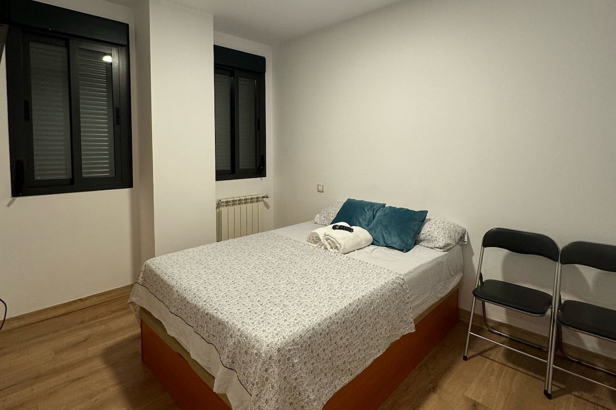 Une chambre avec un lit simple, un radiateur, une fenêtre avec des stores et un luminaire au plafond.