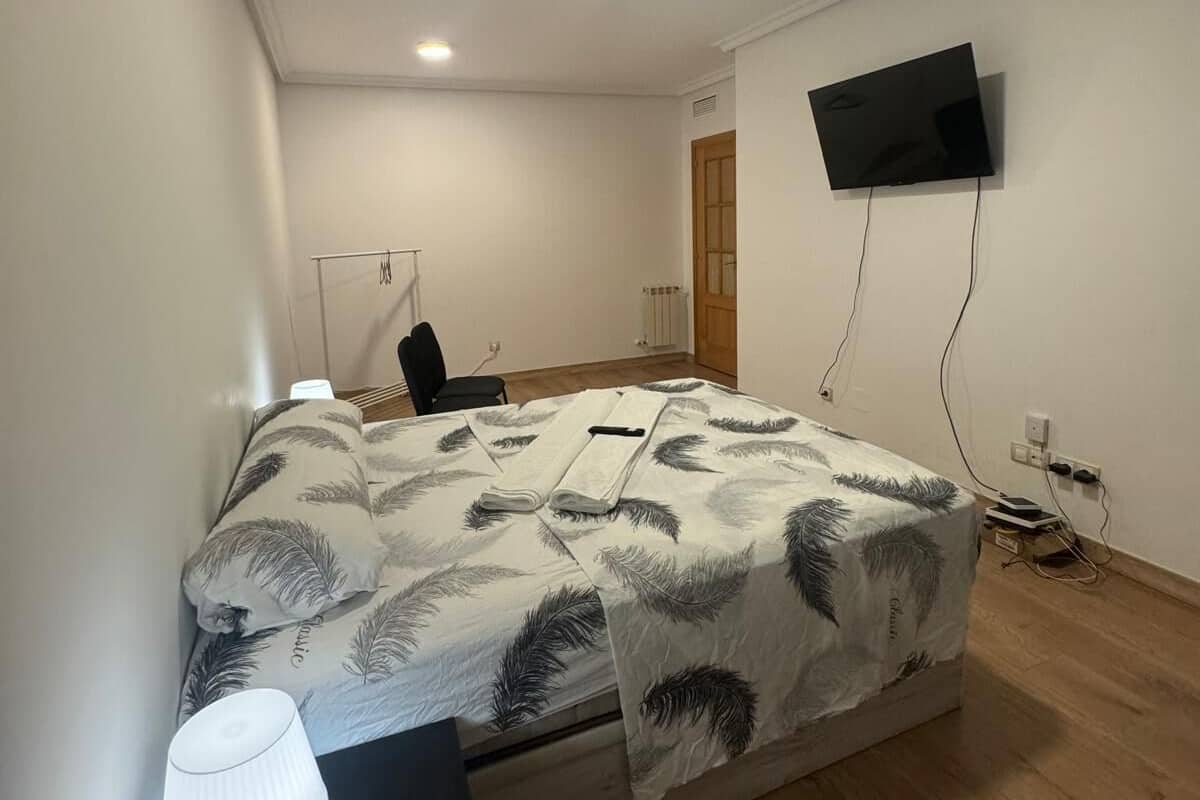 Une chambre à coucher comprenant un lit, un bureau, une chaise, un téléviseur fixé au mur et une porte.