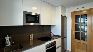 A modern kitchen with white cabinets, a stainless steel microwave, a sink, and a built-in oven. - Mars Suites Zapata  (Madrid)