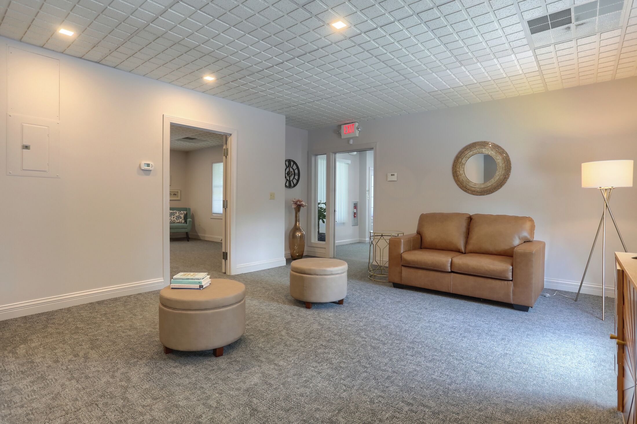 Une pièce spacieuse avec un canapé en cuir beige, deux poufs, une lampe sur pied et un miroir au mur.