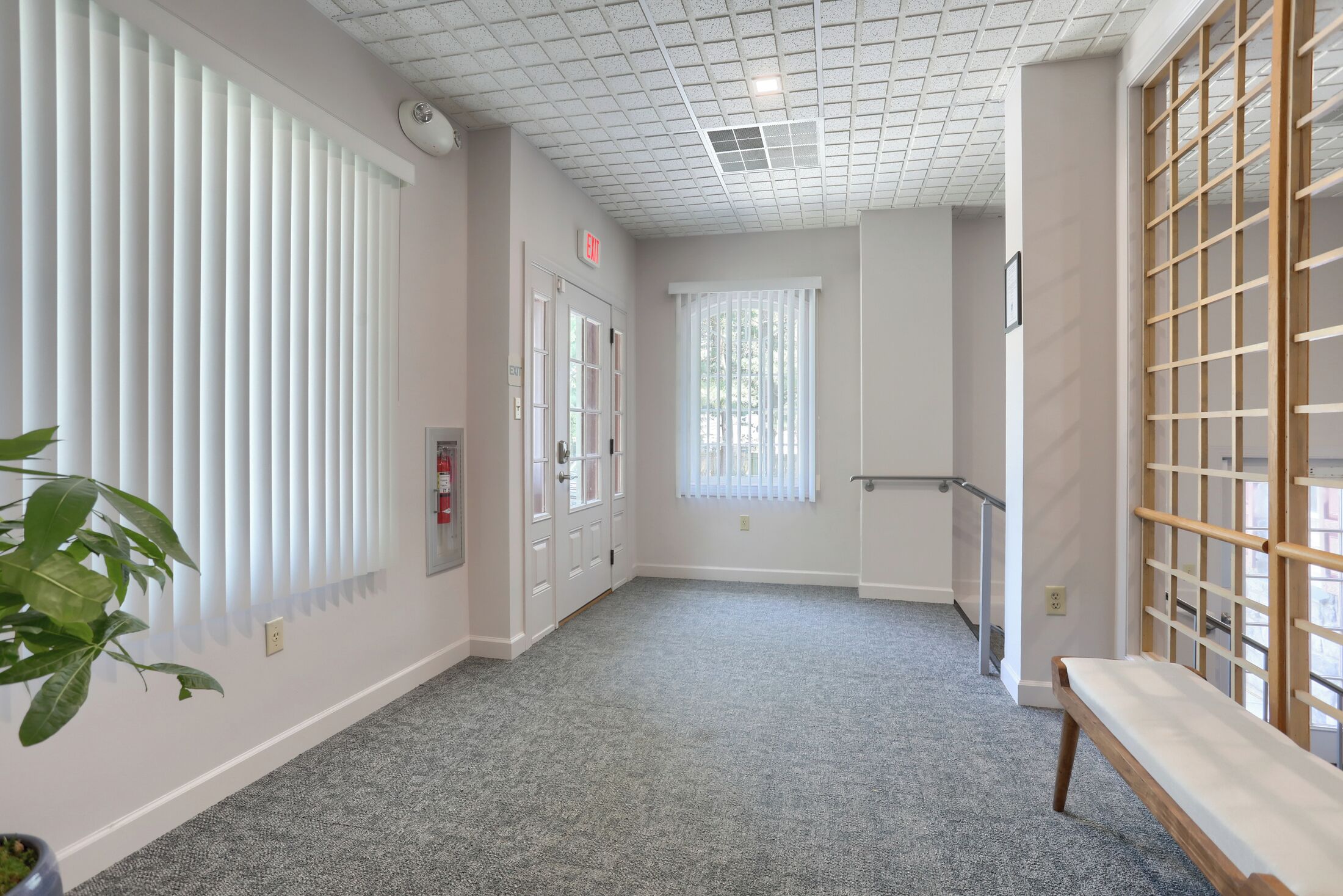 A hallway with a bench, a wooden screen, and a door with an exit sign.