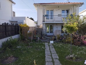 Een tweelaags huis met een balkon, een tuin met een grindpad en een houten omheining.