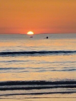 Een zonsondergang boven de oceaan met golven en een persoon in het water.