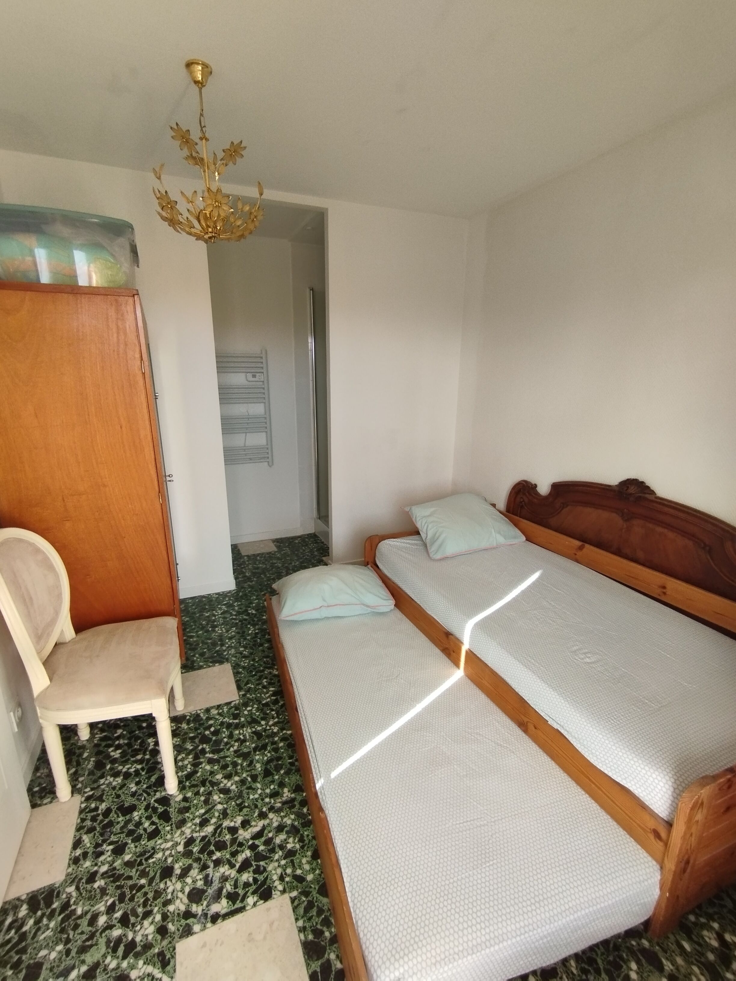 Una habitación con dos camas de madera, una silla de madera, un armario de madera y un suelo con estampado verde y blanco.