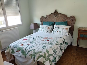 Een opgemaakt bed met bloemenbeddengoed, een houten hoofdbord en een nachtkastje met een lamp.