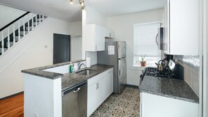 A modern kitchen with granite countertops, white cabinetry, a stainless steel refrigerator, and a gas stove. - Walk to Main St! Spacious 2BR Bi-Level • Sleeps 8 (Philadelphia)