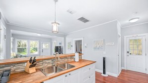 A modern kitchen with a wooden countertop, stainless steel sink, and white cabinetry. - Uptown Escape – Sleeps 6, Pet & Family Friendly (St. Augustine)