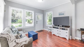 A living room with a sofa, ottoman, TV stand, and windows. - Uptown Escape – Sleeps 6, Pet & Family Friendly (St. Augustine)