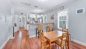 A modern kitchen with white cabinets, a central island, and a dining area with a wooden table and chairs. - Uptown Escape – Sleeps 6, Pet & Family Friendly (St. Augustine)
