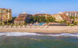 A beachfront hotel with multiple balconies, a pool area, and a sandy beach.