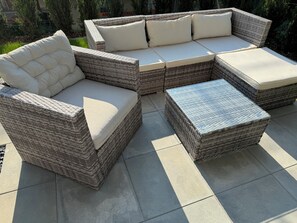 A wicker sectional sofa with cushioned seats and a matching ottoman. - Moderne, Ruhige Gartenwohnung mit Gemütlicher Terrasse Zwischen Stadt und Natur (Oberrüti)