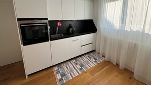 A modern kitchen with white cabinets, a black countertop, a built-in oven, a sink, and a patterned rug.