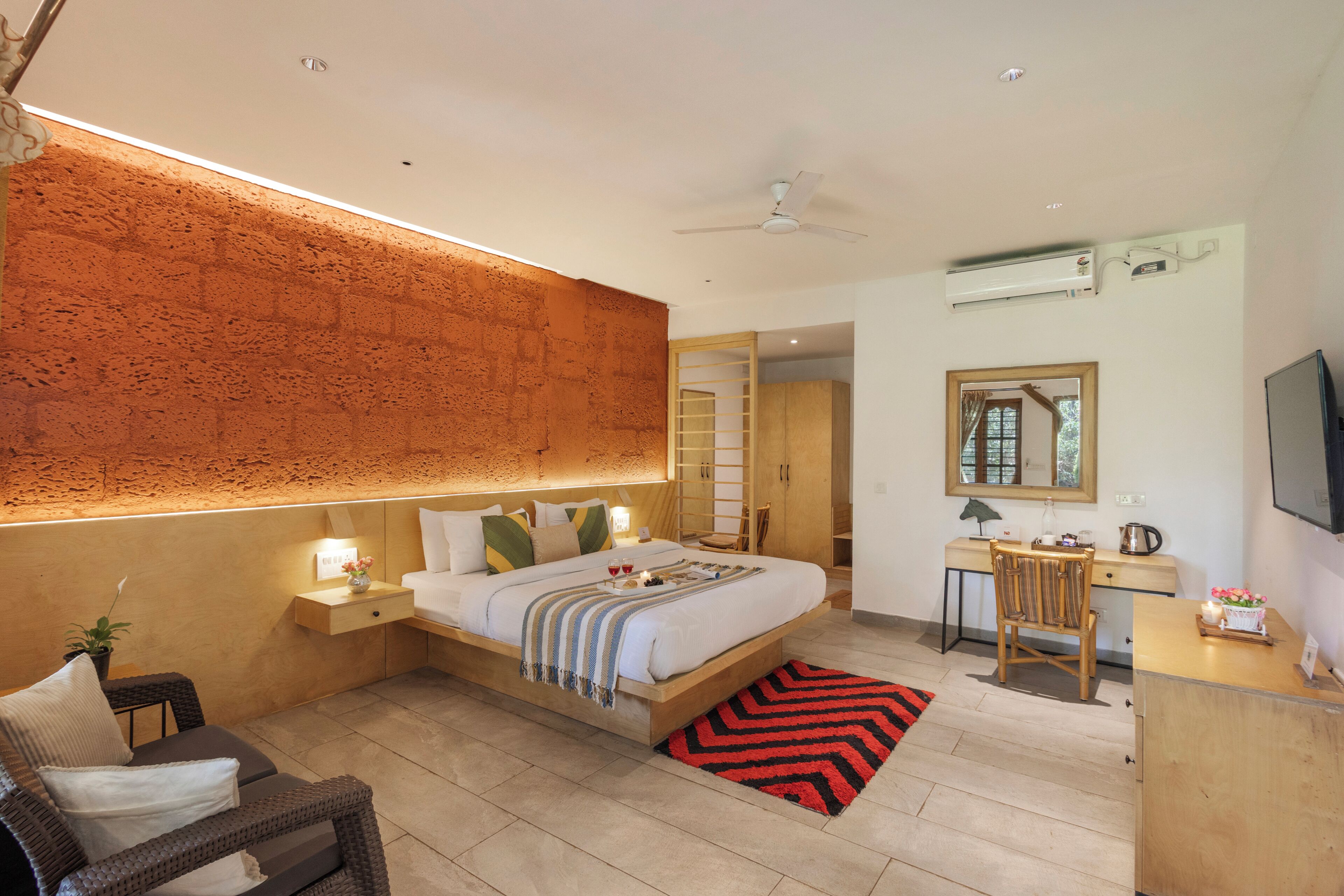A modern hotel room with a bed, bedside table, chair, desk, and a flat-screen TV.