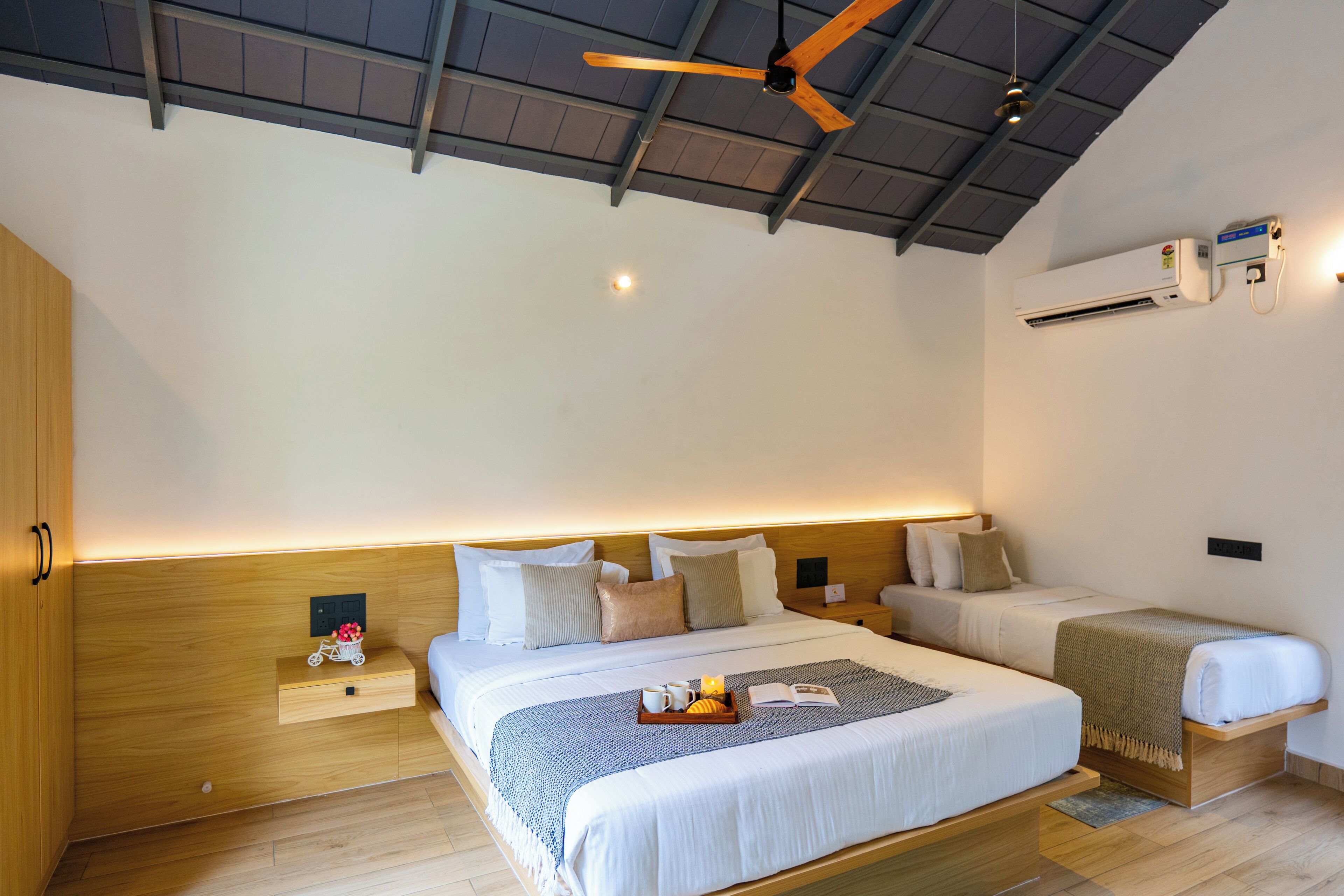 Une chambre d’hôtel moderne dotée d’un grand lit, d’un lit plus petit, d’un ventilateur de plafond, d’un appareil de climatisation et d’une table de chevet avec une lampe.
