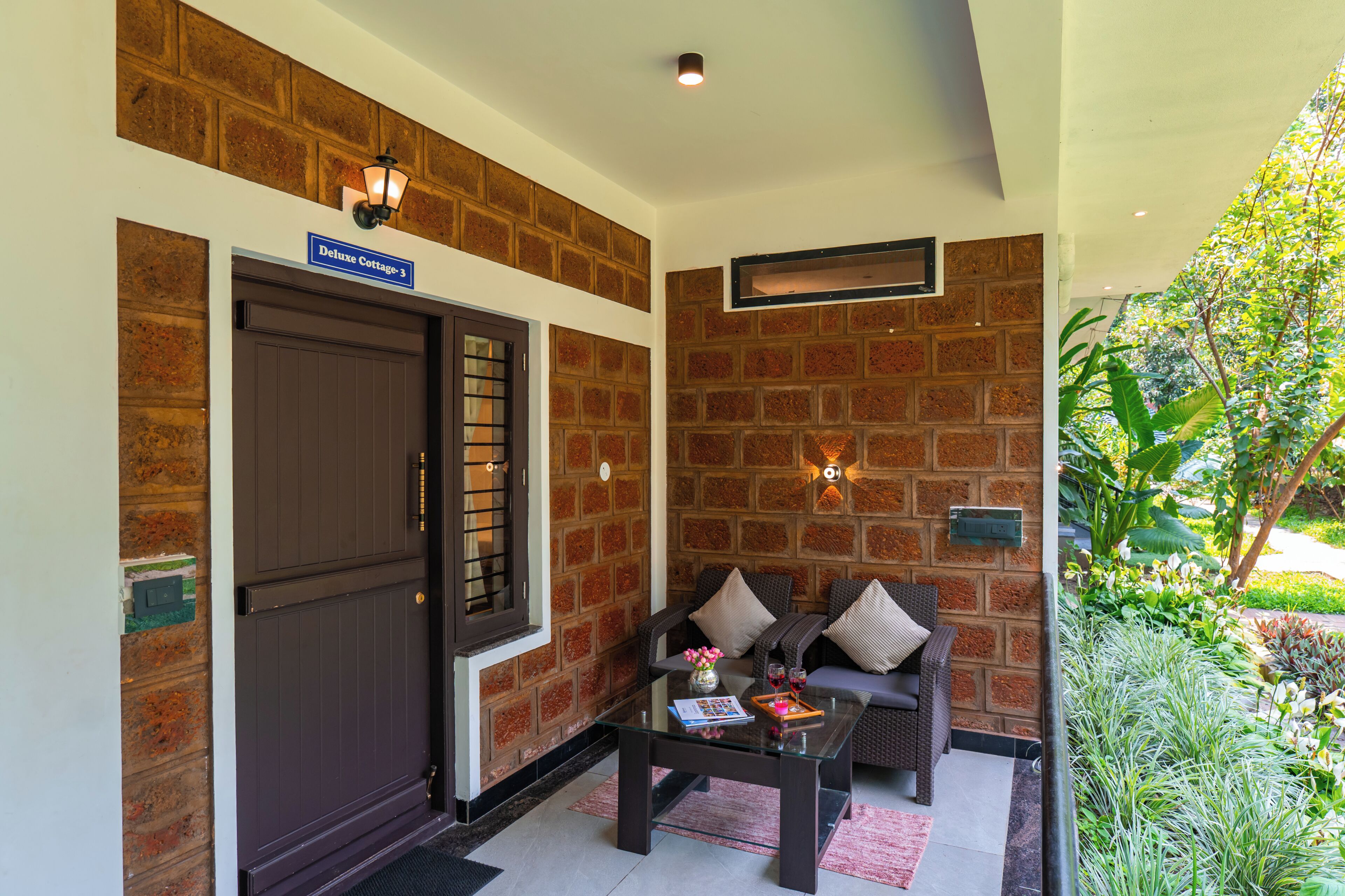A brick wall, a dark door, a glass table with a book and a vase, and a sofa with cushions.