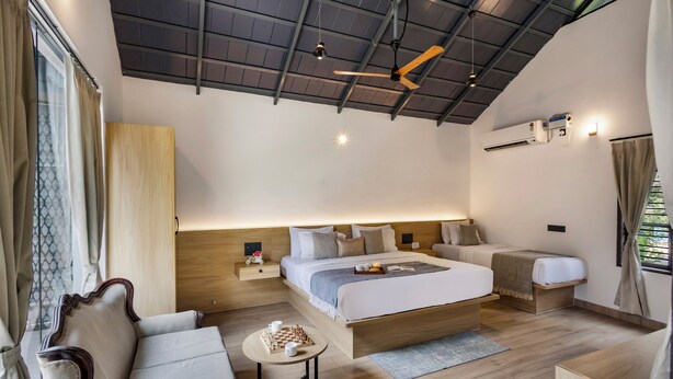 A modern bedroom with a large bed, bedside tables, a desk, a chair, and a ceiling fan. - Avocado Cottages by Alaya stays (Somvarpet)