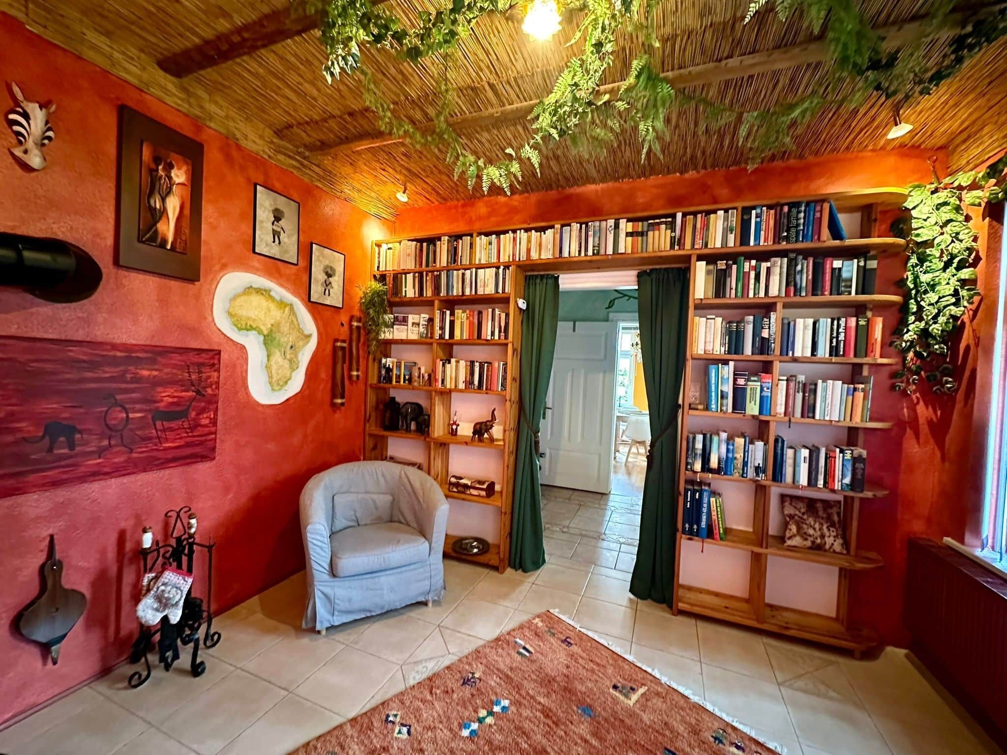 Ein gemütliches Zimmer mit Bücherregal, einem Sessel und einer Karte an der Wand.