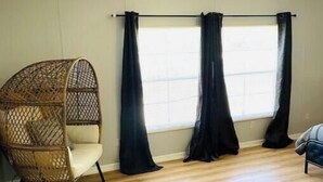Una habitación con piso de madera, un sillón colgante y una ventana con cortinas negras.