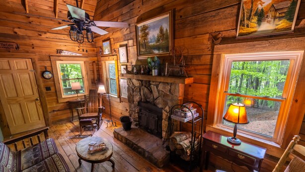 Ein gemütliches Blockhaus-Interieur mit Holzwänden, einem Kamin aus Stein, einem Essbereich und einem großen Fenster mit Blick auf einen Wald.