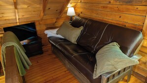 Ein Holzhütten-Interieur mit einem braunen Ledersofa, einem kleinen Tisch mit Lampe und einem grünen Handtuch auf einem Stuhl.