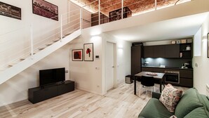 En modern lägenhet med en trappa som leder upp till ett loft, ett matområde och ett vardagsrum med en grön soffa.