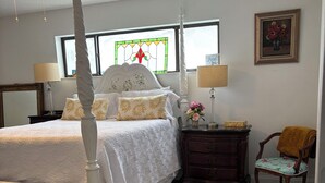 A bedroom with a four-poster bed, a nightstand with a lamp, a chair, and a wooden dresser.