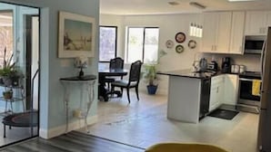 A modern kitchen with white cabinets, a dining area with a table and chairs, and a yellow chair in the foreground.