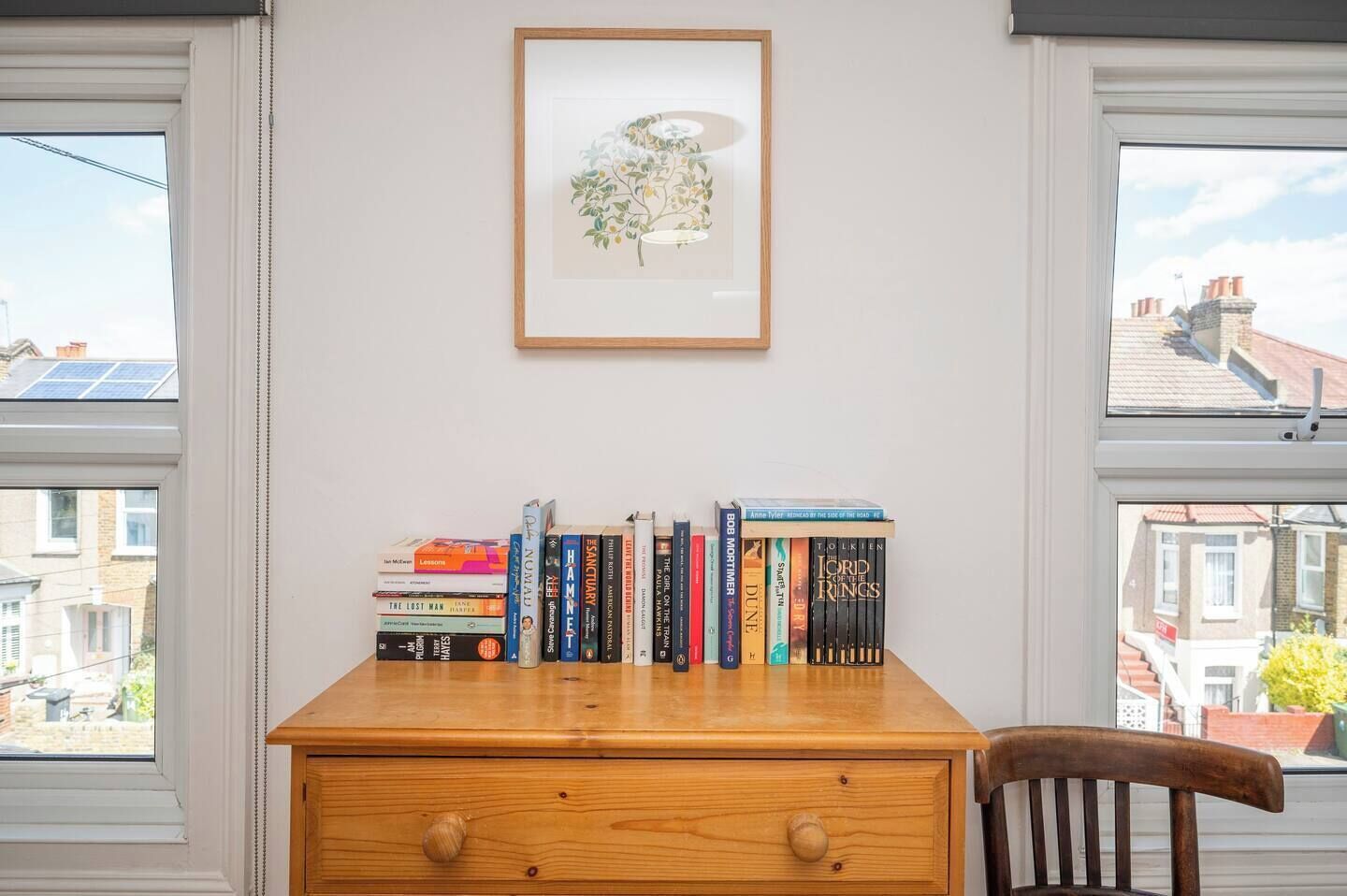 Ein Holztisch mit einem Stapel Bücher, einem gerahmten Bild und Blick auf eine Wohngegend durch Fenster.