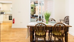 A dining area with a wooden table and chairs, a fire extinguisher, and a view of the outside through a glass door.