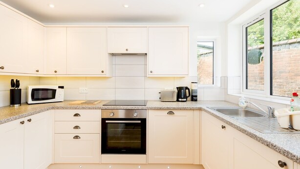 A modern kitchen with white cabinets, a built-in oven, a microwave, and a window with a view of greenery.