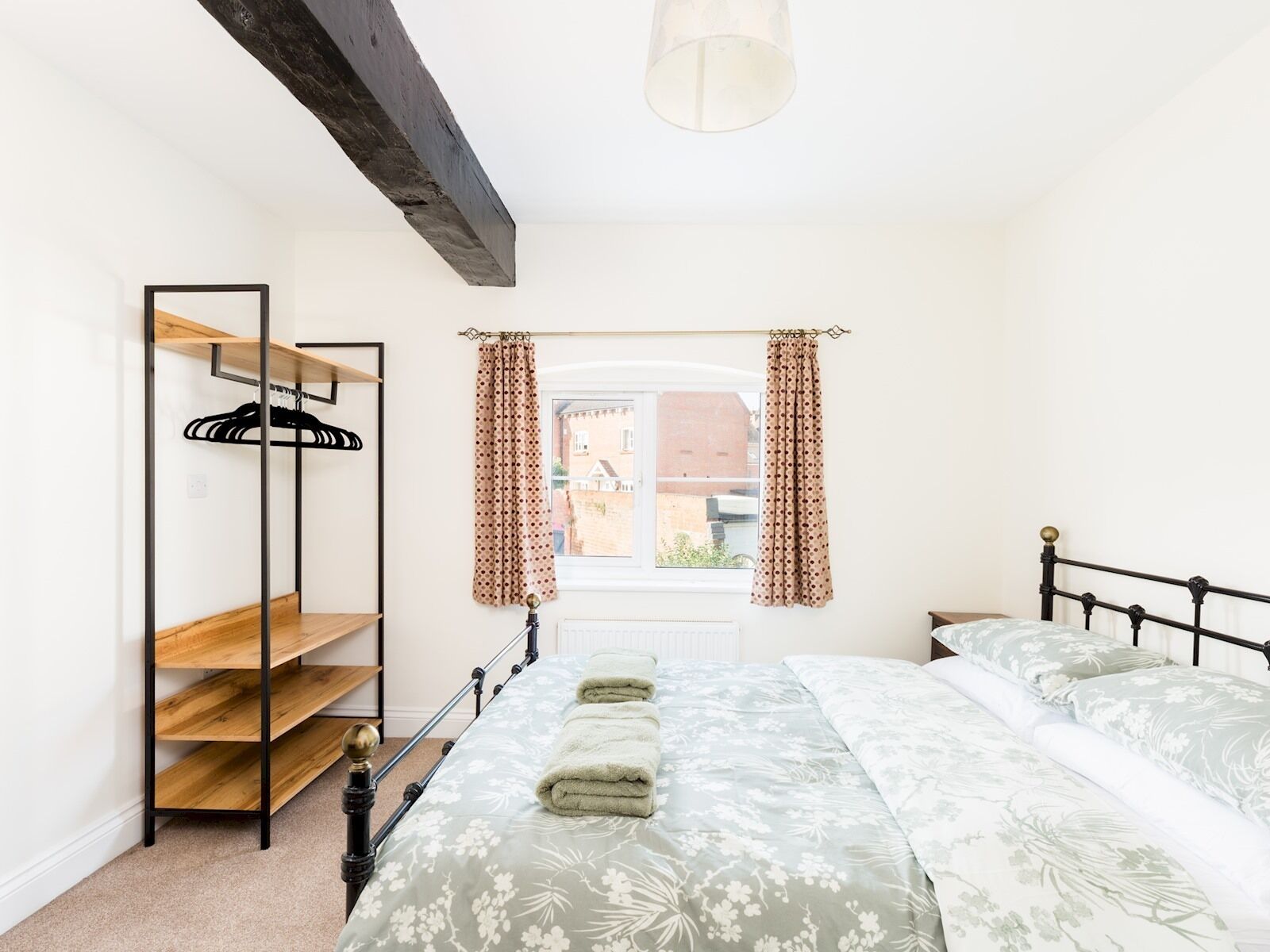 Un dormitorio con cama, estantería de madera y ventana con cortinas.