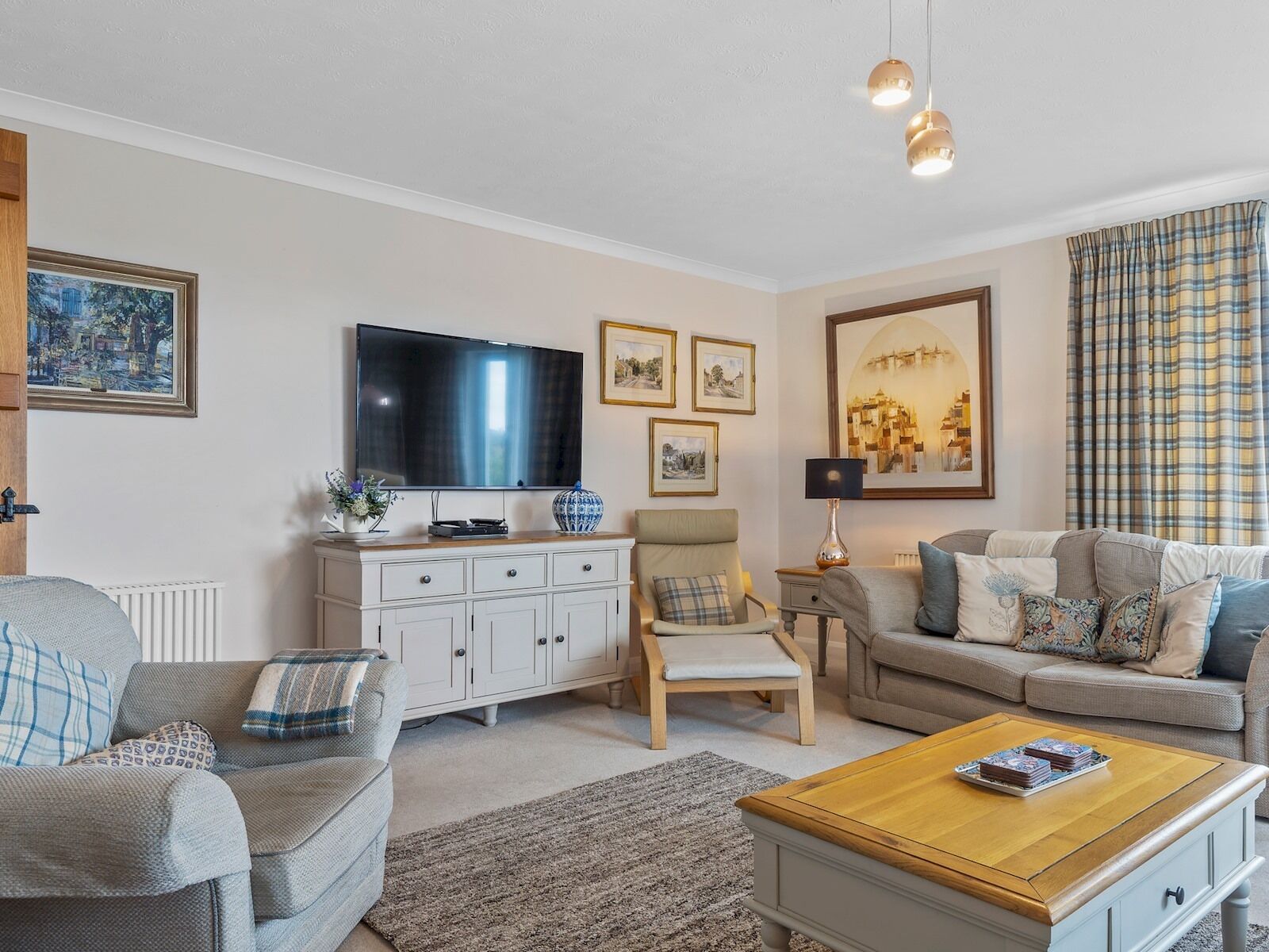 A living room with a television, sofa, armchair, coffee table, and artwork on the walls.