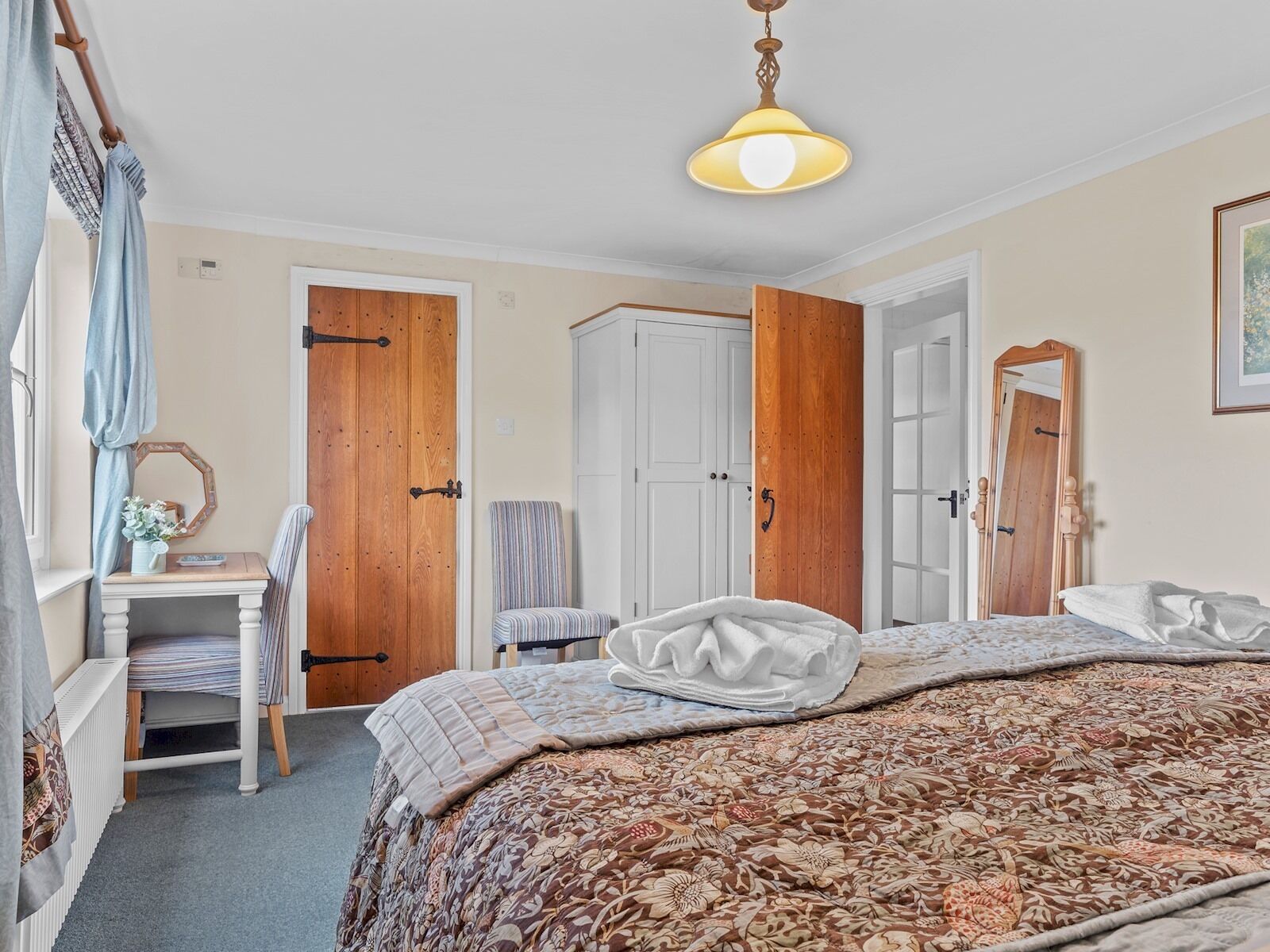 A bedroom with a large bed, a chair, a desk, and a wardrobe.