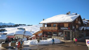 A wooden building with a sign reading "Superdry®" and a snow-covered mountain in the background. - 50m from ski slopes, 1st floor, terrace, fireplace or stove, tv, 72m², Les Saisies (Hauteluce)
