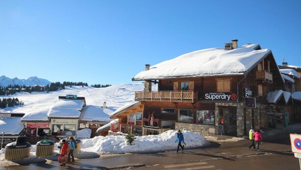 A wooden building with a sign reading "Superdry®" and a snow-covered mountain in the background.