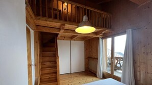 A wooden cabin bedroom with a bed, a staircase, and a large window. - 50m from ski slopes, 1st floor, terrace, fireplace or stove, tv, 72m², Les Saisies (Hauteluce)