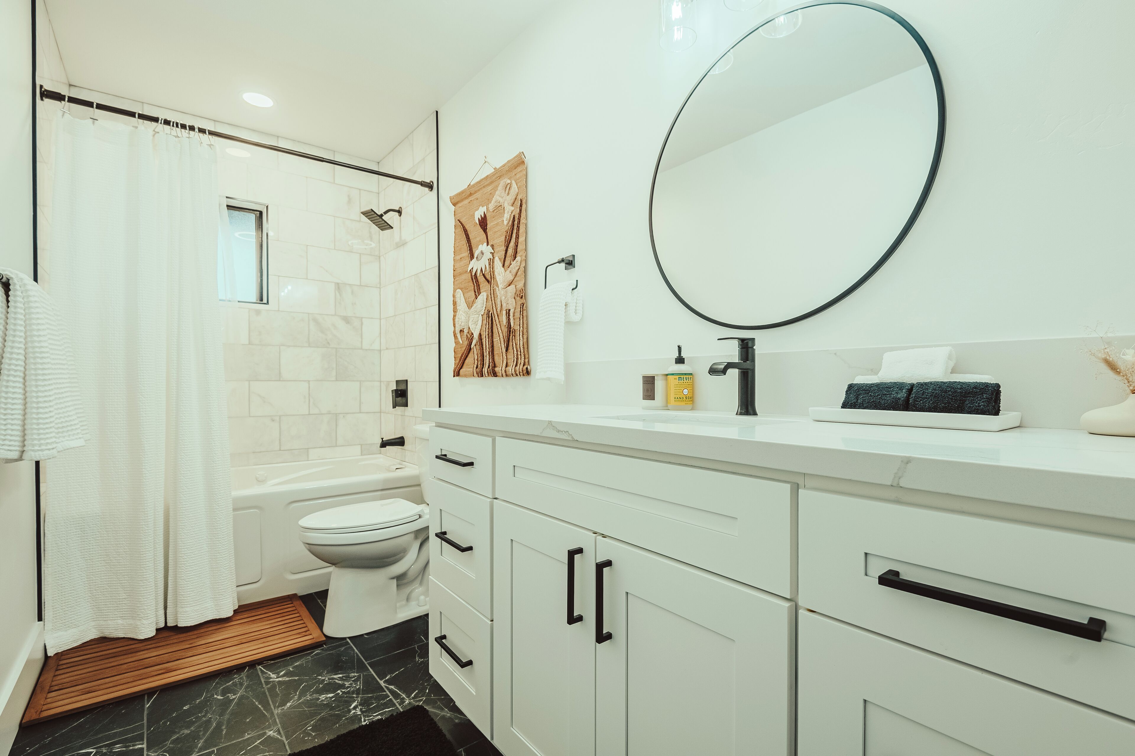 Une salle de bain moderne avec un meuble-lavabo blanc, un miroir rond, des toilettes et un espace douche.