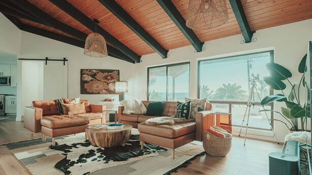 A spacious living room with a large window, a wooden ceiling, and a cozy seating area with leather sofas and a round coffee table.