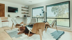 A modern kitchen with a dining area, large windows, and a flat-screen TV.