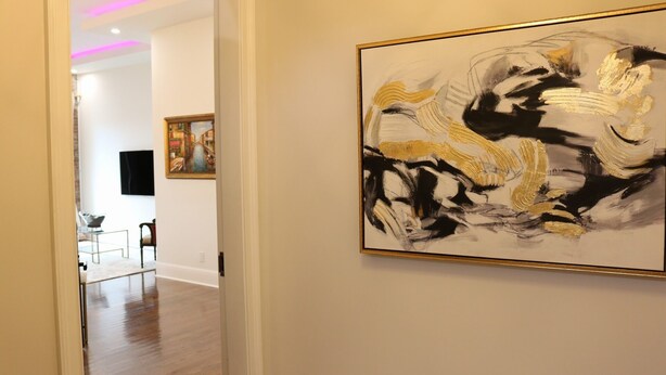Un pasillo con una obra de arte moderno en la pared, un comedor con mesa y sillas, y un televisor montado.