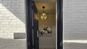 A black door leading into a room with a tiled floor and a black mat at the entrance. A white brick wall with a number sign and a painting are visible. - The Luxe High Roller! 2 bed apt in Metropolis near Harrah's Casino! Pet friendly (Metropolis)