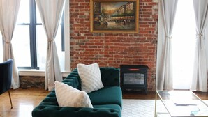 Un salon chaleureux avec un canapé vert, une cheminée et une grande fenêtre agrémentée de rideaux.