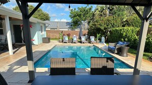 Un patio trasero con piscina, sillones de descanso y un porche techado.